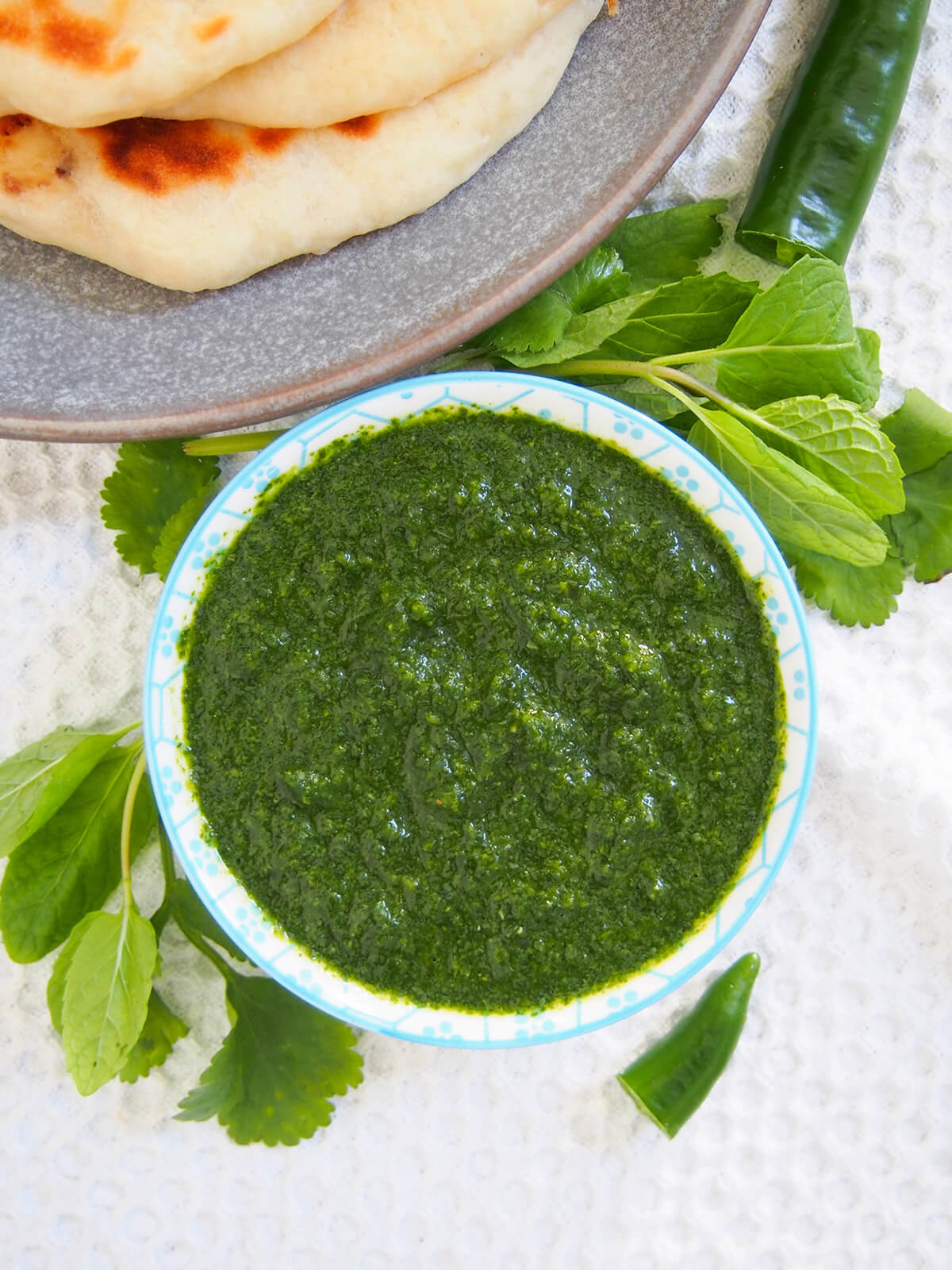 small bowl of cilantro mint chutney from overhead with herbs to side