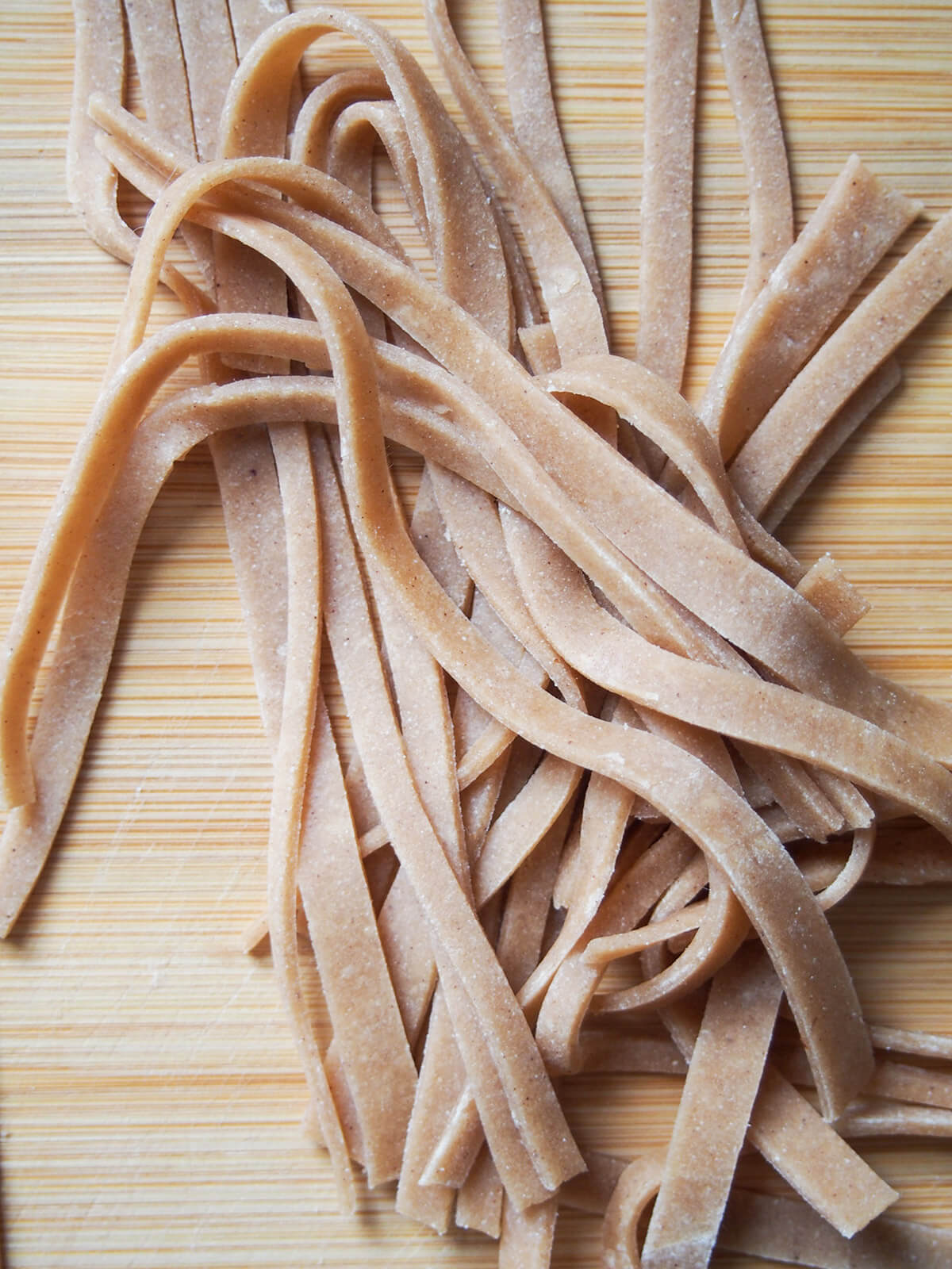 strips of uncooked chestnut pasta strips of cut pasta dough on cutting board.