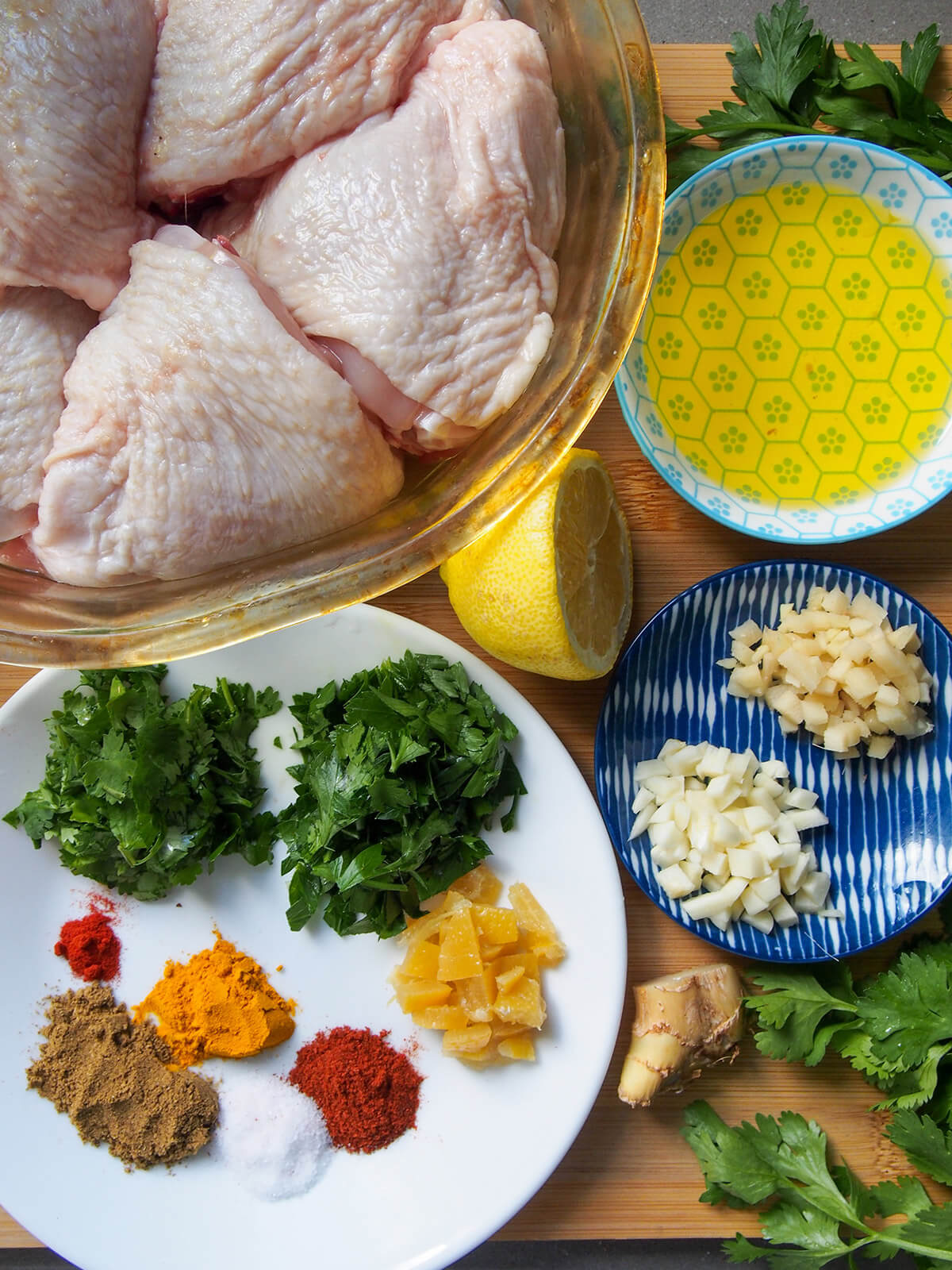 bowl with chicken thighs, plates with herbs and spices and olive oil
