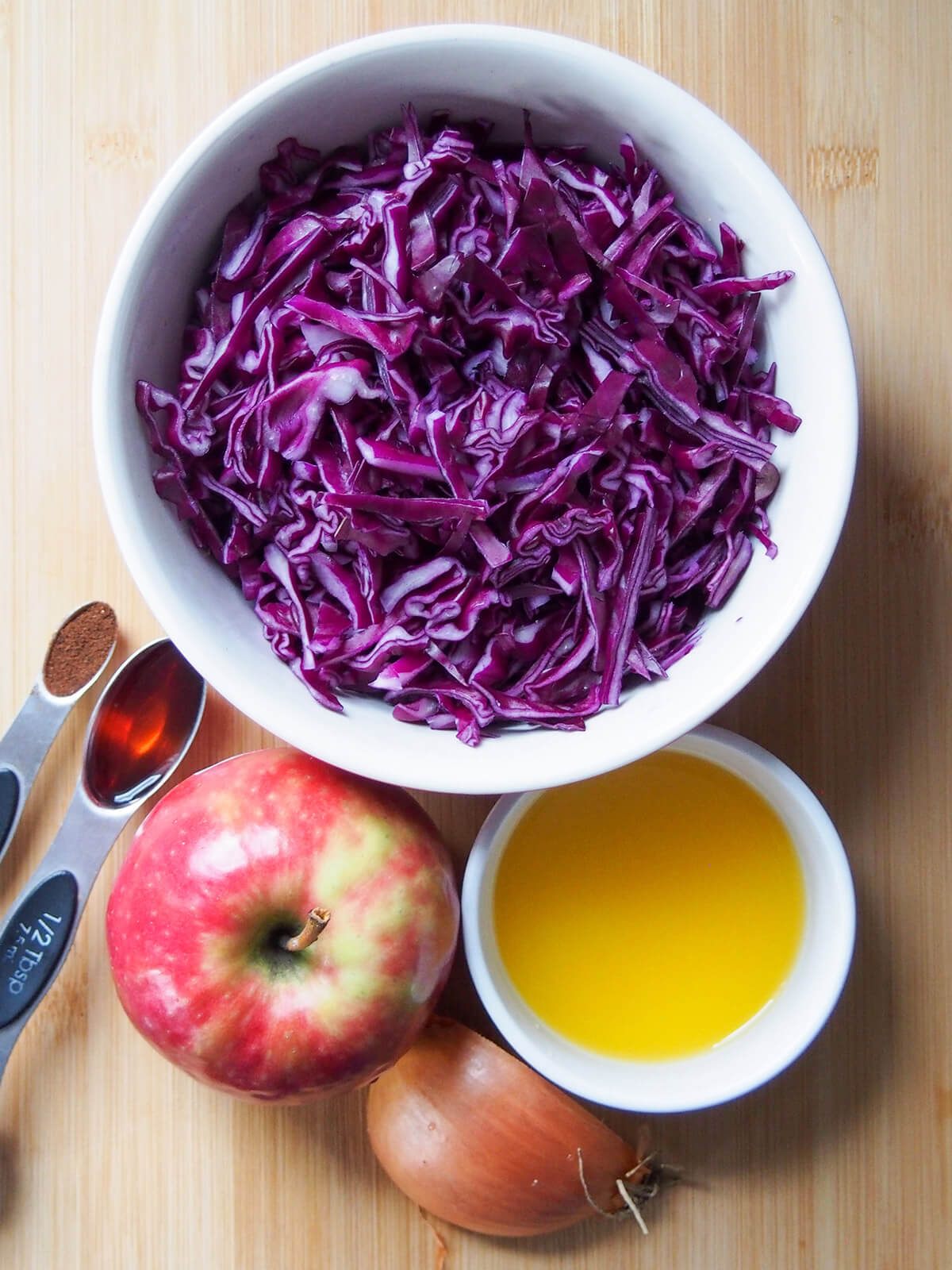 bowls with red cabbage, orange juice, an apple, part onion and spoons of vinegar and cloves to side