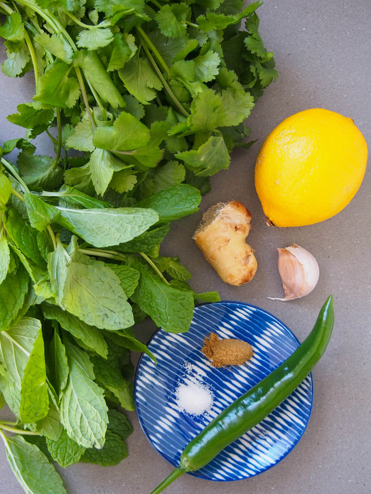 bunches of cilantro and mint with chili, garlic, ginger and lemon to side and spices on small plate