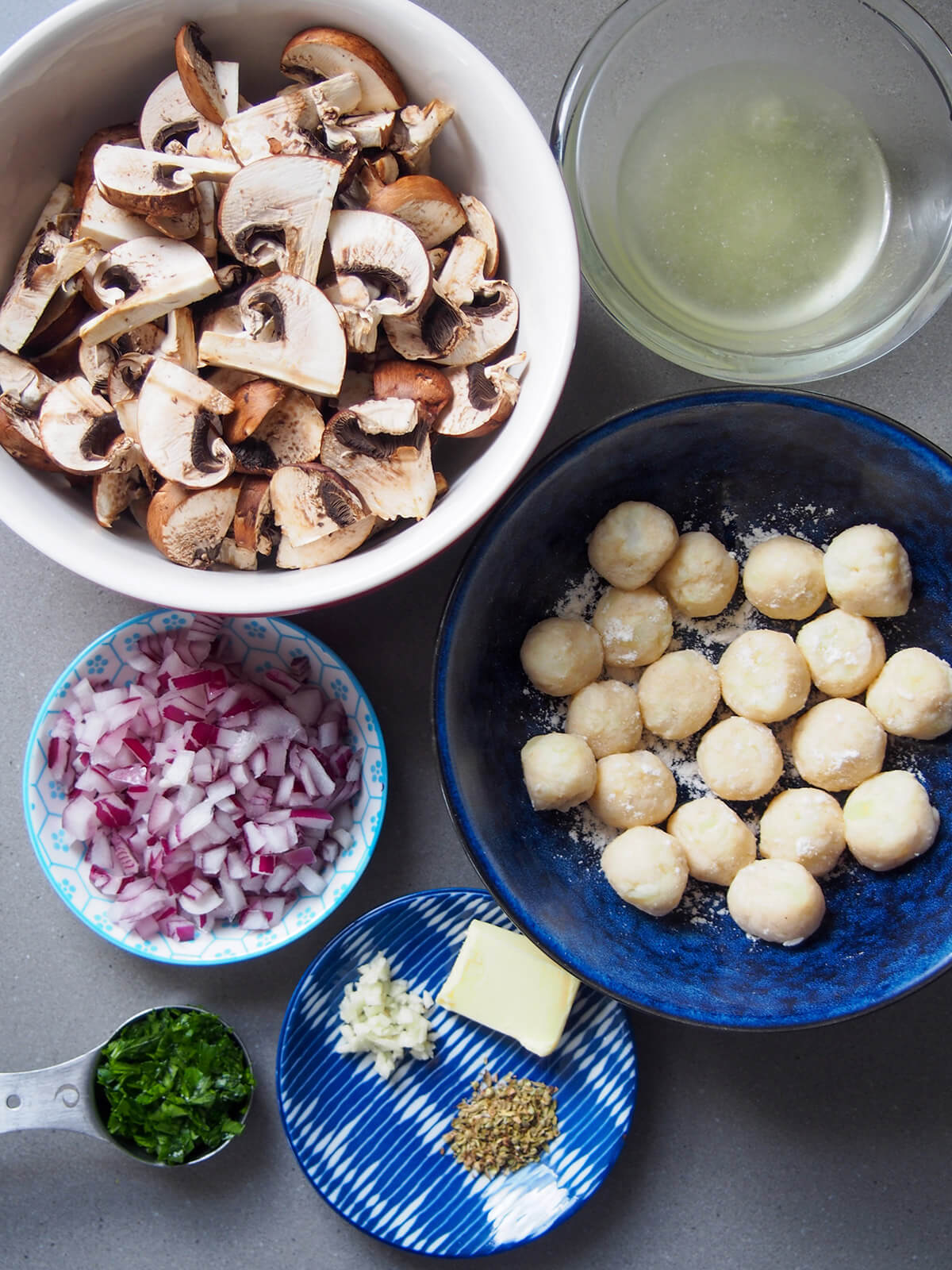 bowls with mushrooms, gnocchi, stock, chopped onions and to bottom garlic, thyme and butter on plate and spoon of parsely