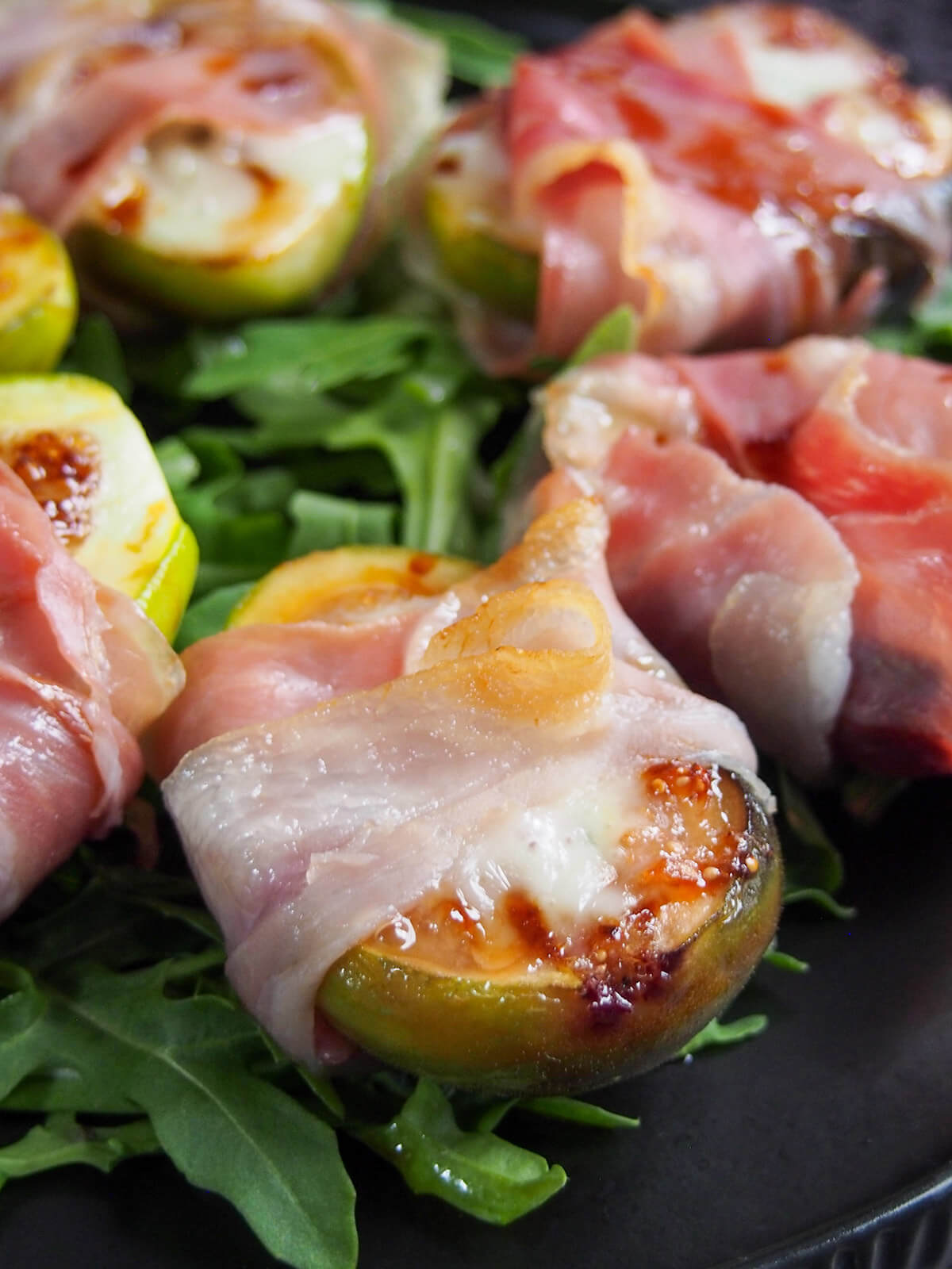 close up of prosciutto wrapped fig with more behind and to side
