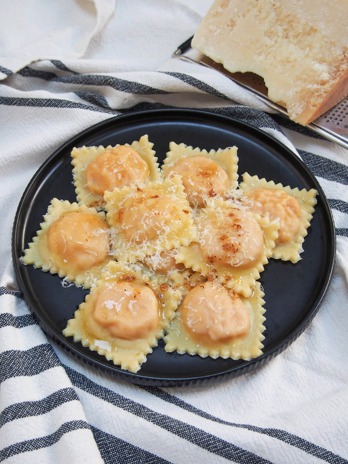 plate of sweet potato ravioli with chunk of parmesan behind plate