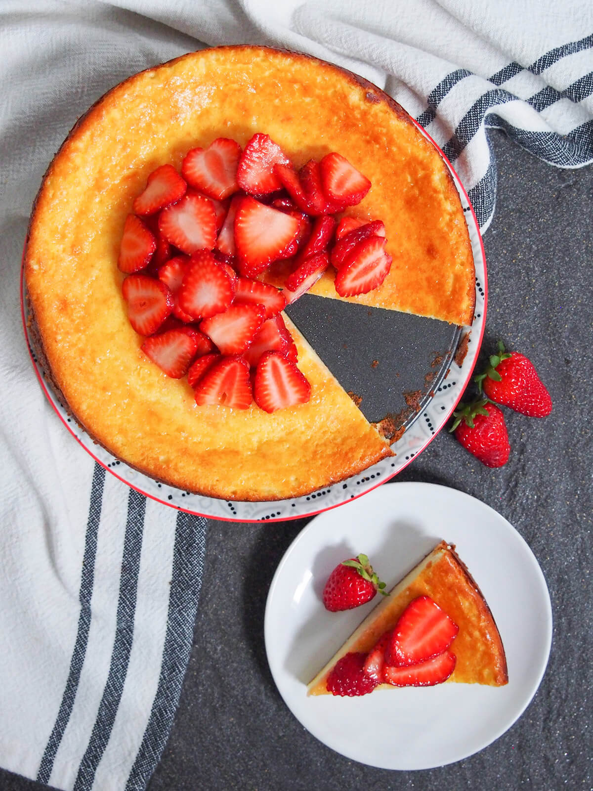 overhead view of Swedish cheesecake ostkaka topped with strawberries aith slice on plate below