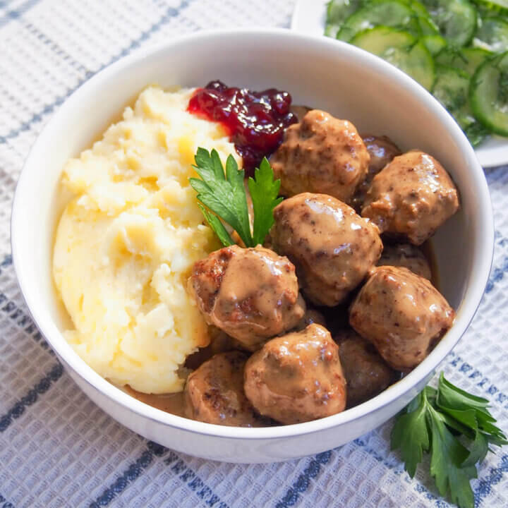 bowl of Swedish meatballs with mashed potato and lingonberries behind