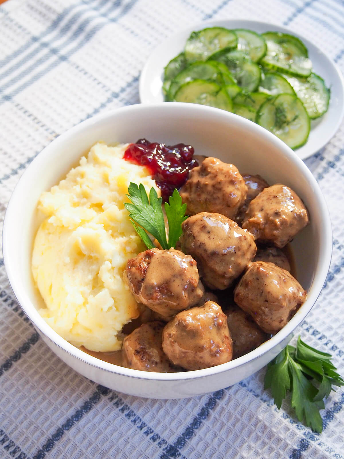 bowl of Swedish meatballs and mashed potatoes with plate of pressed cucumber behind