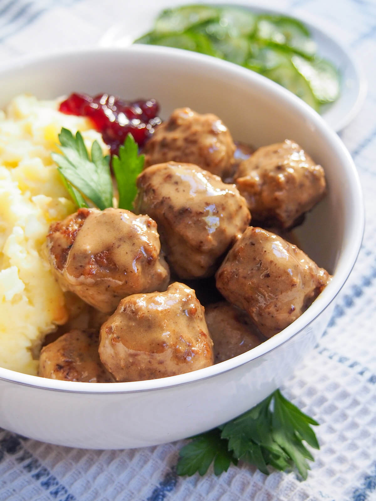 side view of meatballs with creamy sauce over them and lingonberries showing behind