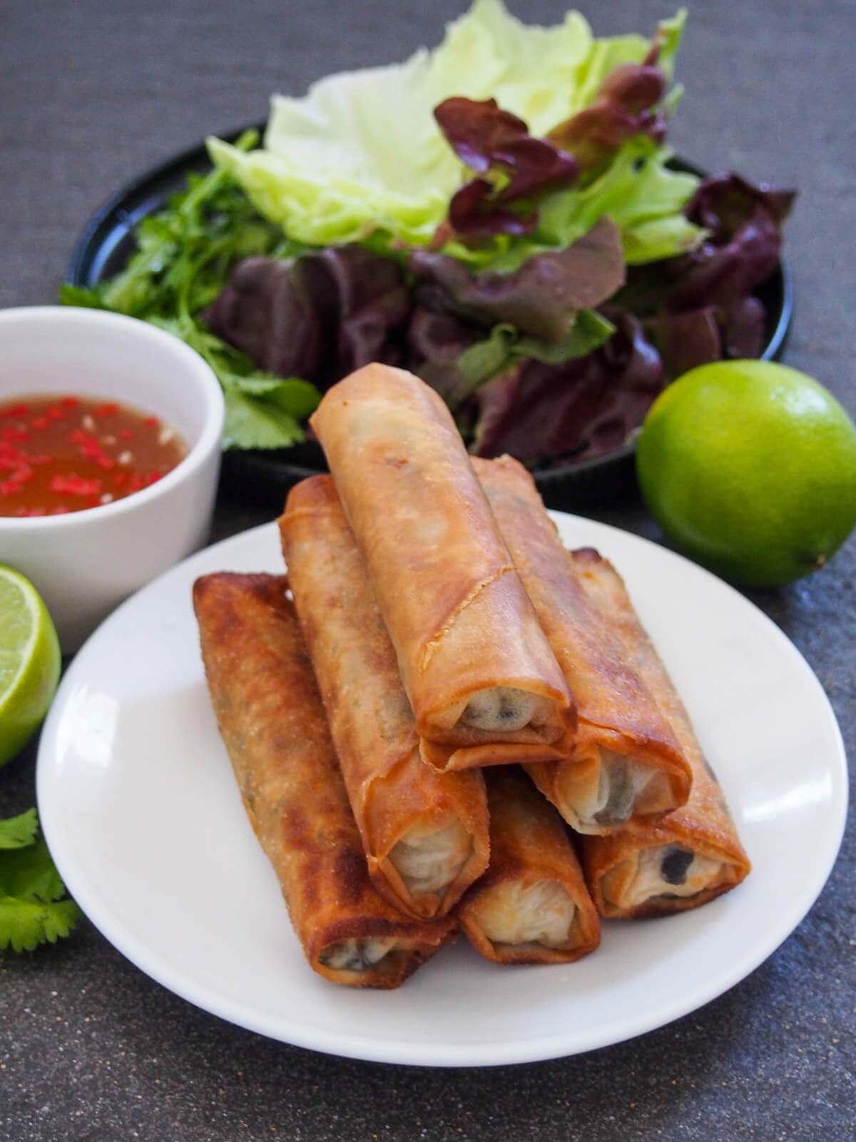 plate of Vietnamese fried spring rolls with lettuce leaves behind and lime and bowl of nuam choc to sides