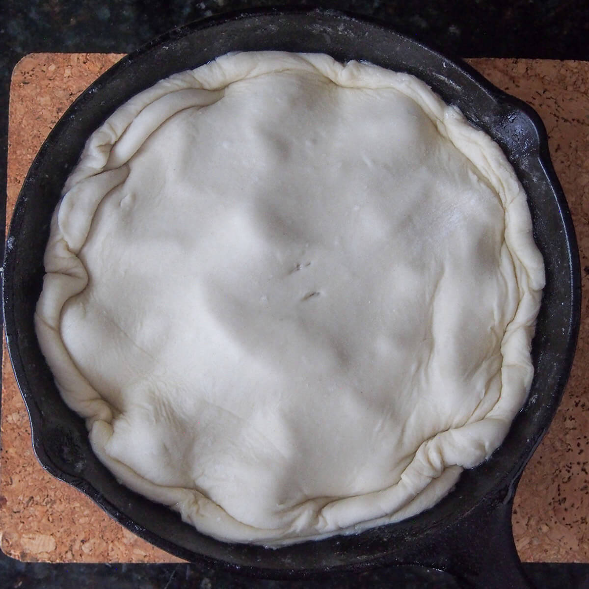 adding pastry to tarte tatin pastry over top of of skillet with apples under before baking