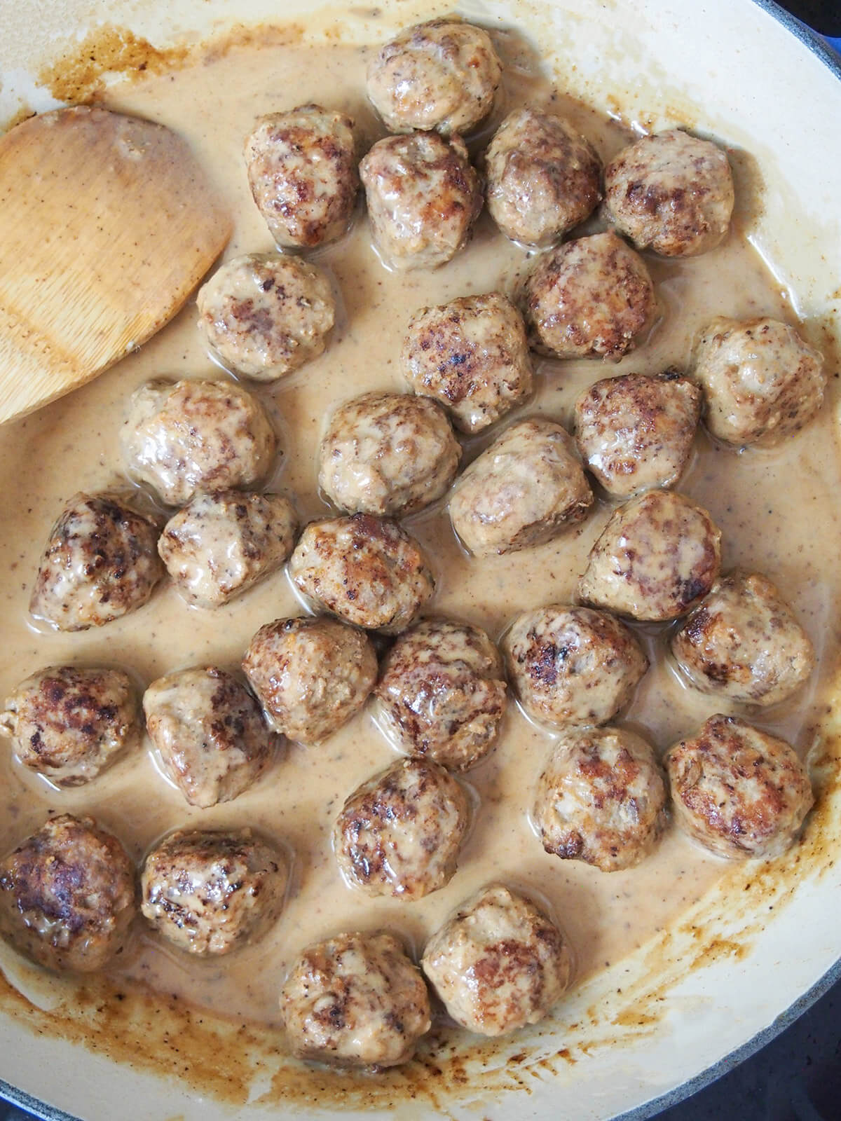 stirring meatballs in cream sauce in dish viewed from overhead