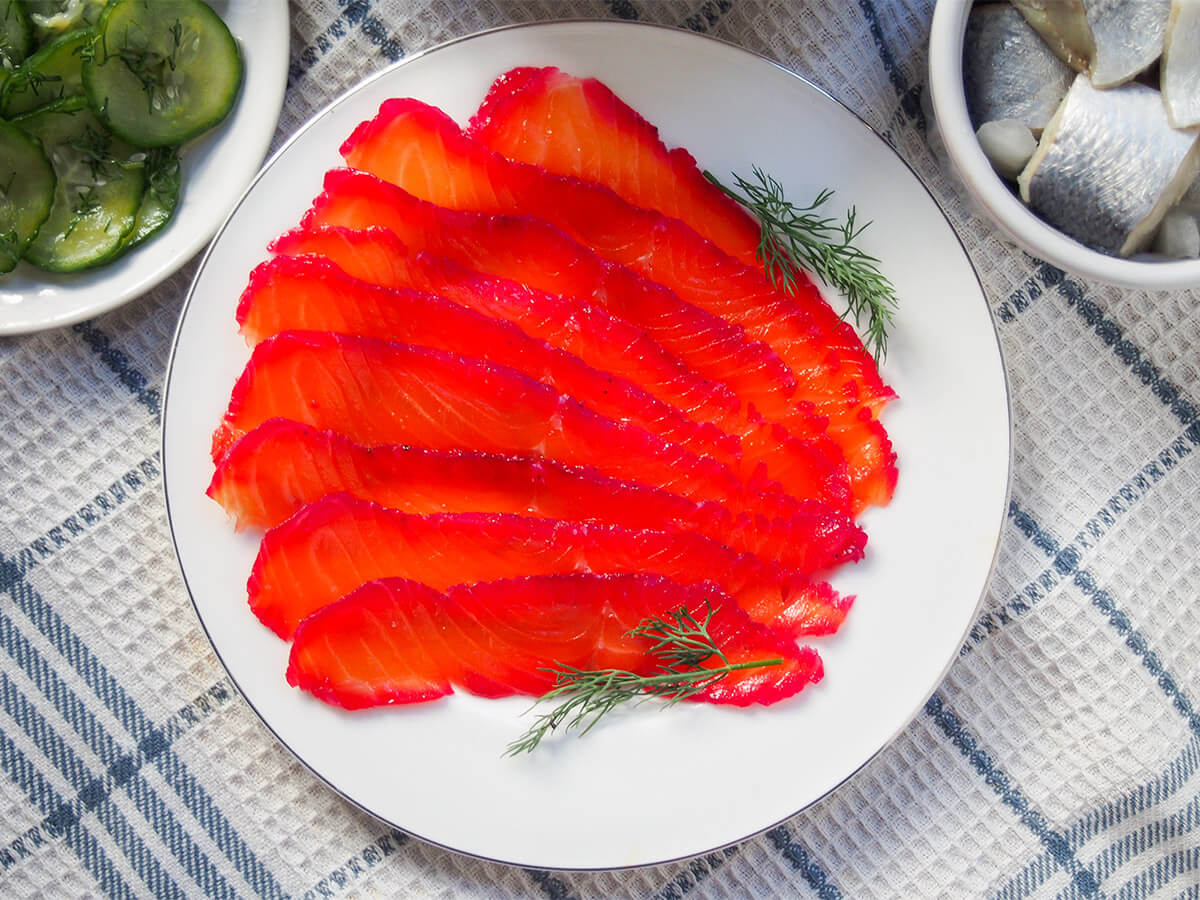 This beet cured salmon is a simple twist on gravlax where the salmon takes on a beautiful purple hue on the one side. Yes, you have a little wait, but it's easy to make and the result is delicious and perfect for elegant appetizers. plate of beet cured salmon gravlax with corners of bowls with herring and cucumber