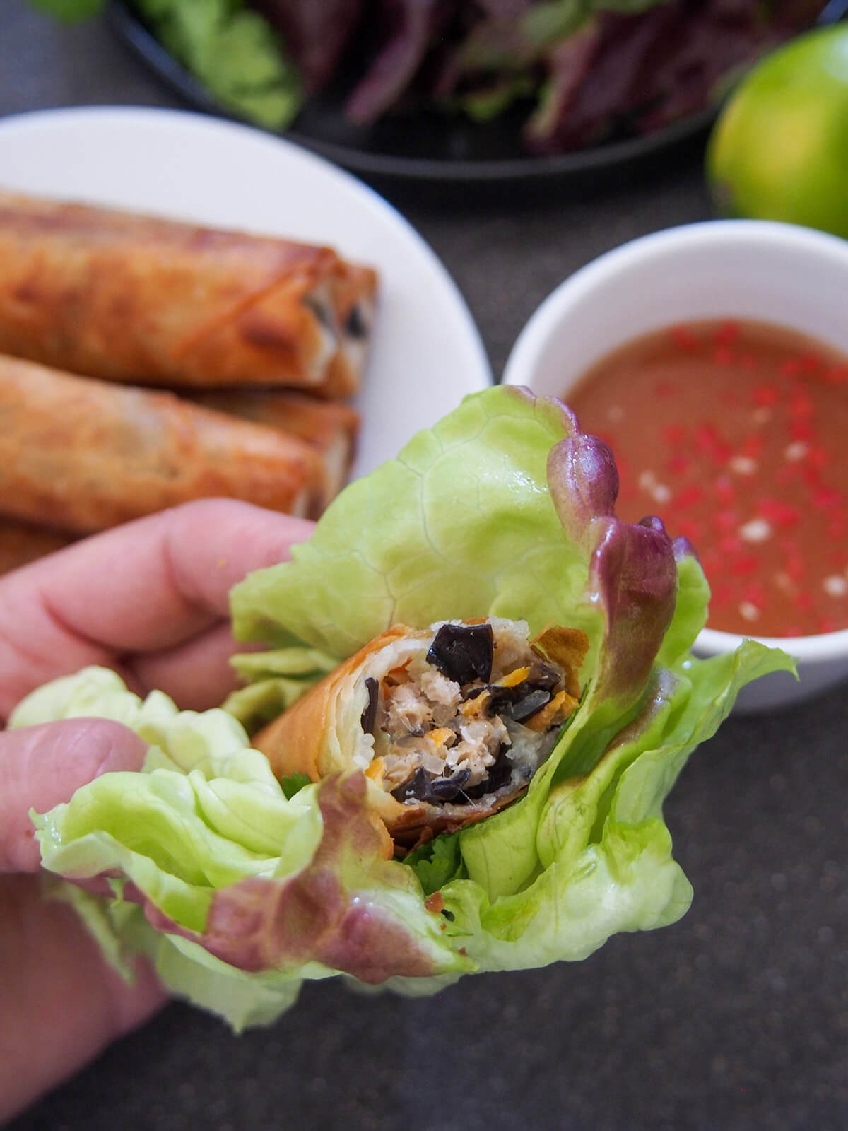 holding bitten Vietnamese fried spring roll in lettuce with bowl of nuoc cham behind