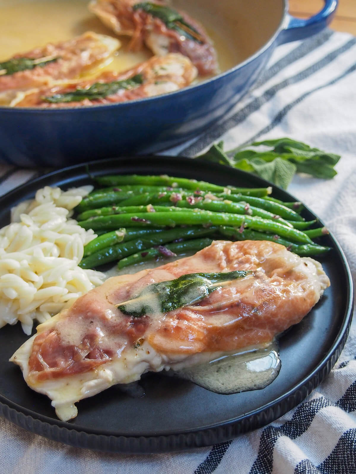 plate of chicken saltimbocca with beans and orzo with additional chicken in pan behind