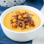 Delicata squash soup topped with curried chickpeas and onions in white bowl
