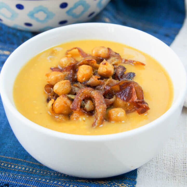 Delicata squash soup topped with curried chickpeas and onions in white bowl