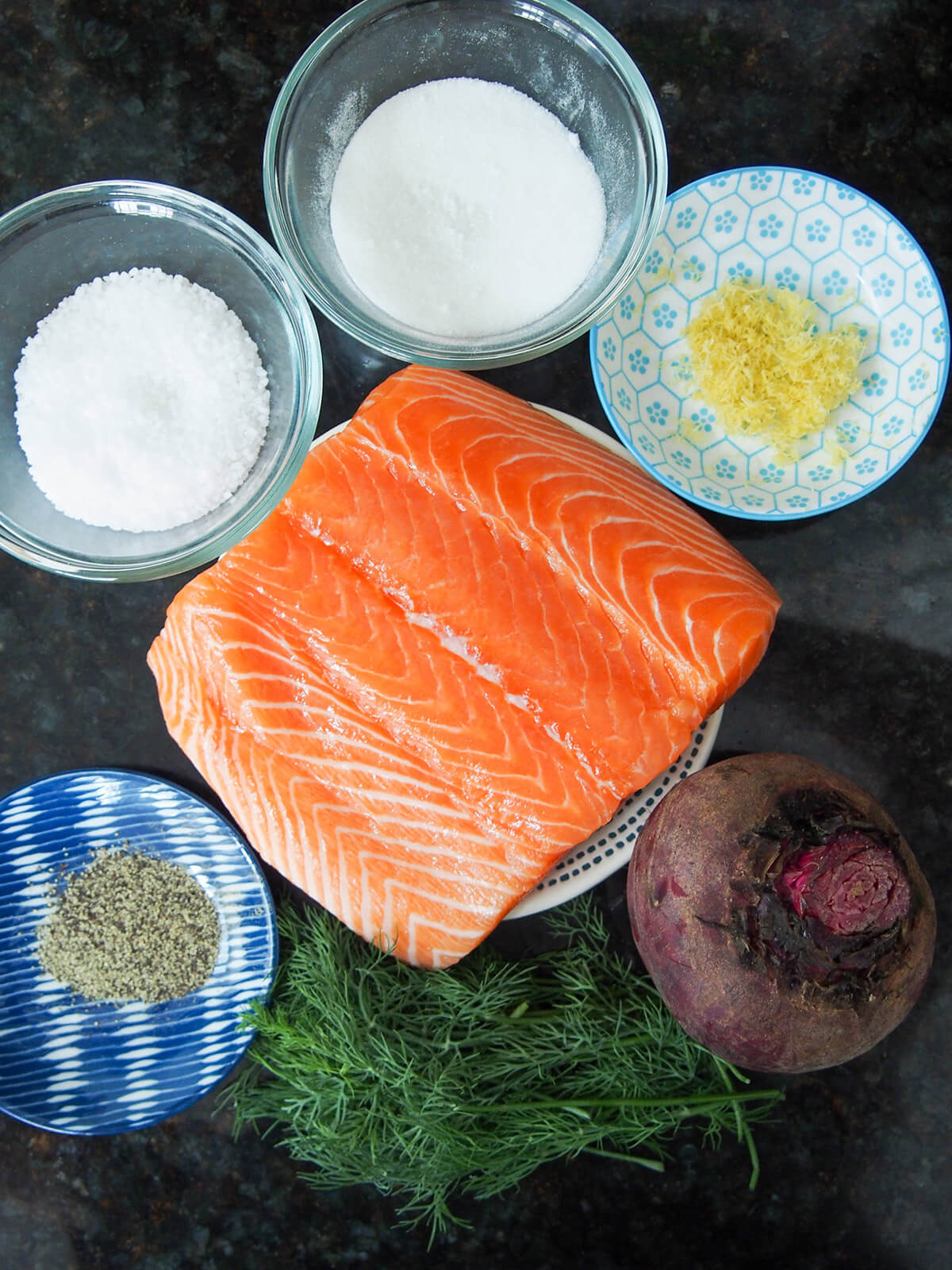 ingredients for beet cured salmon plates with salmon, sugar, salt, lemon zest, pepper with a beet and dill below