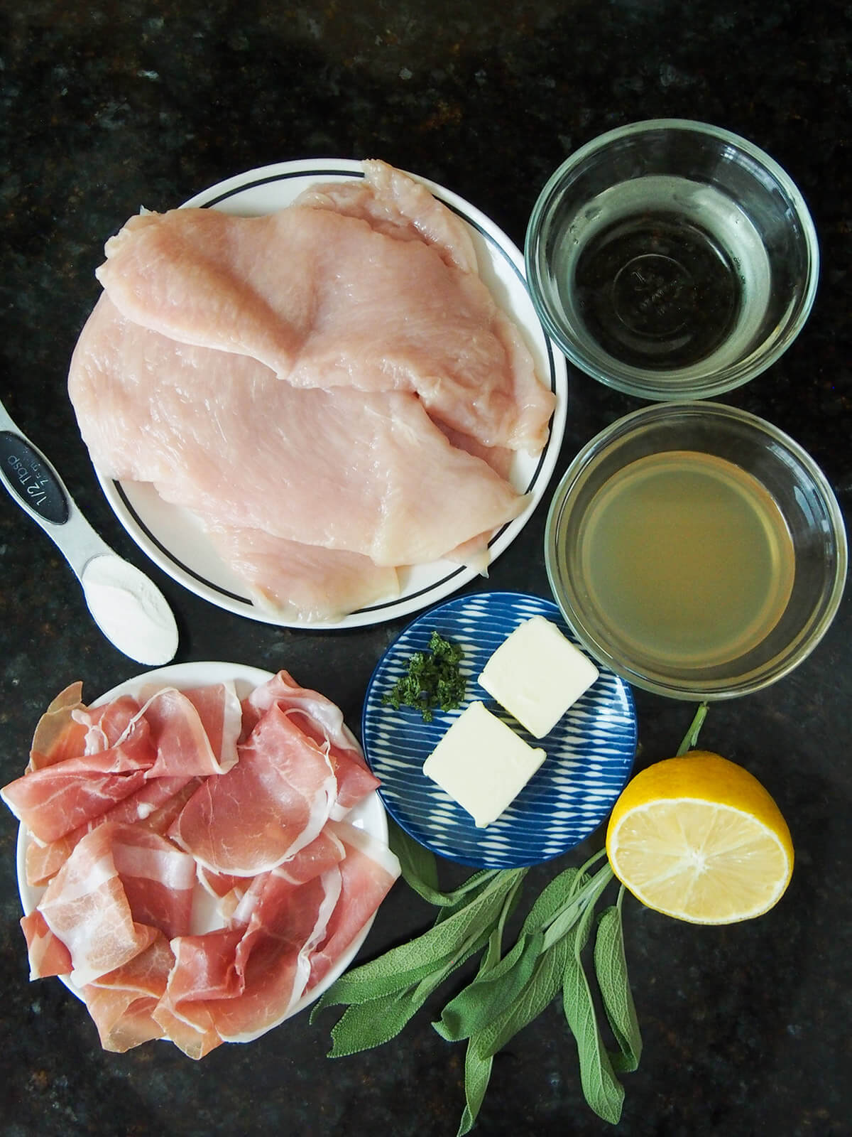 plates with chicken, prosciutto, butter and bowls of wine and stock with sage and lemon to side