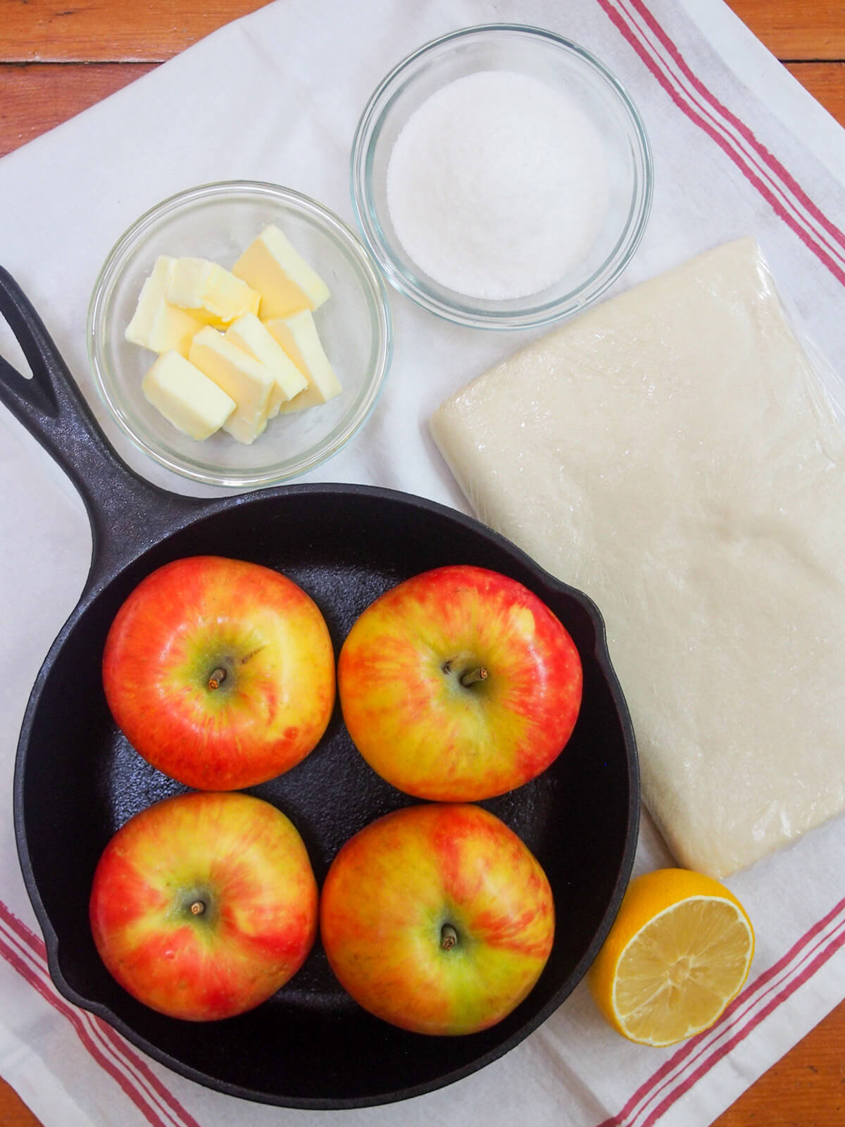 ingredients for classic apple tarte tatin skillet with apples in it, bowls with sugar and butter, pastry and lemon