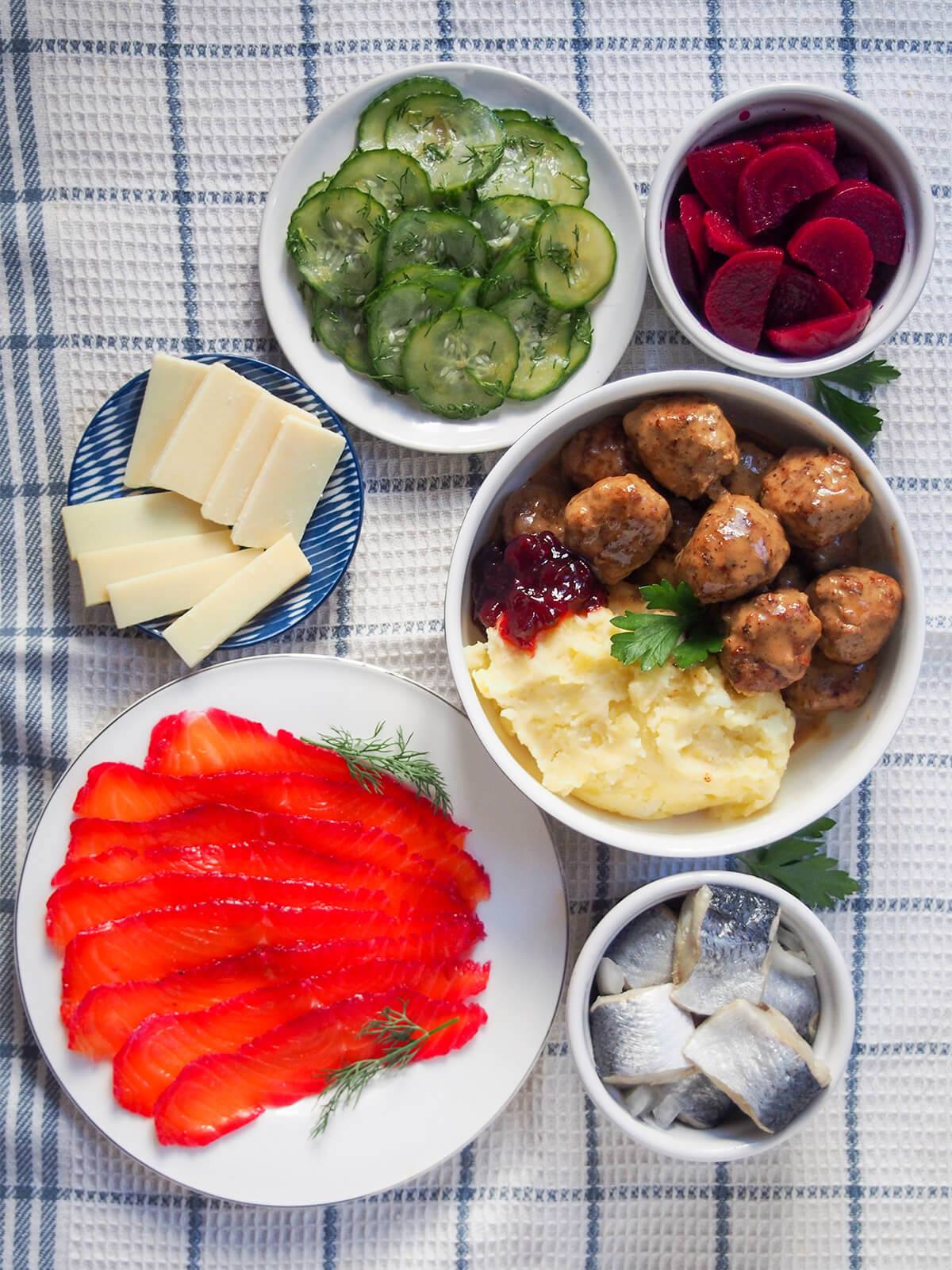 selection of smorgasbord dishes including beet cured salmon and Swedish meatballs overhead view of plates of gravlax, cheese, pressgurka and bowls with pickled beet, herring and meatballs and potato