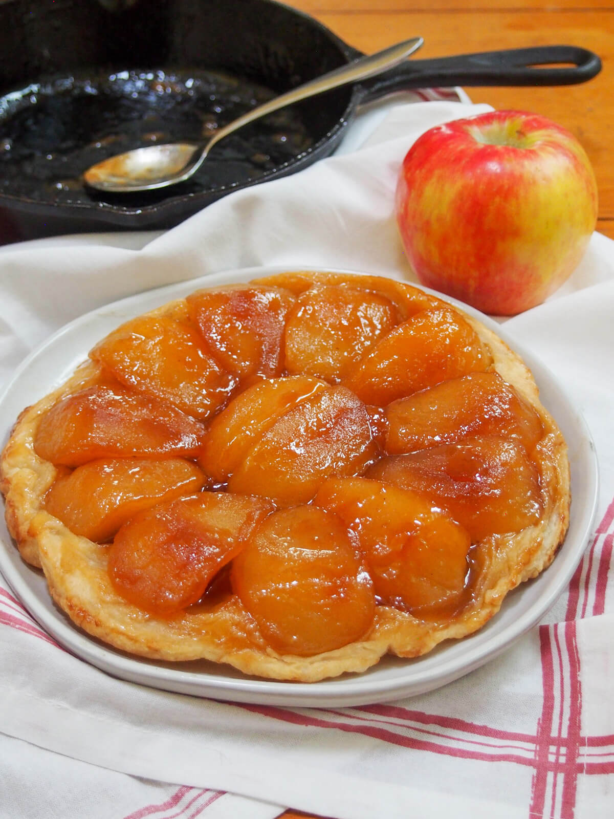 Apple tarte tatin is a classic French dessert that tastes wonderfully indulgent, despite only a few ingredients. An upside down tart with luscious caramel-coated, tender apples and is oh so good. apple tarte tatin on plate with skillet behind