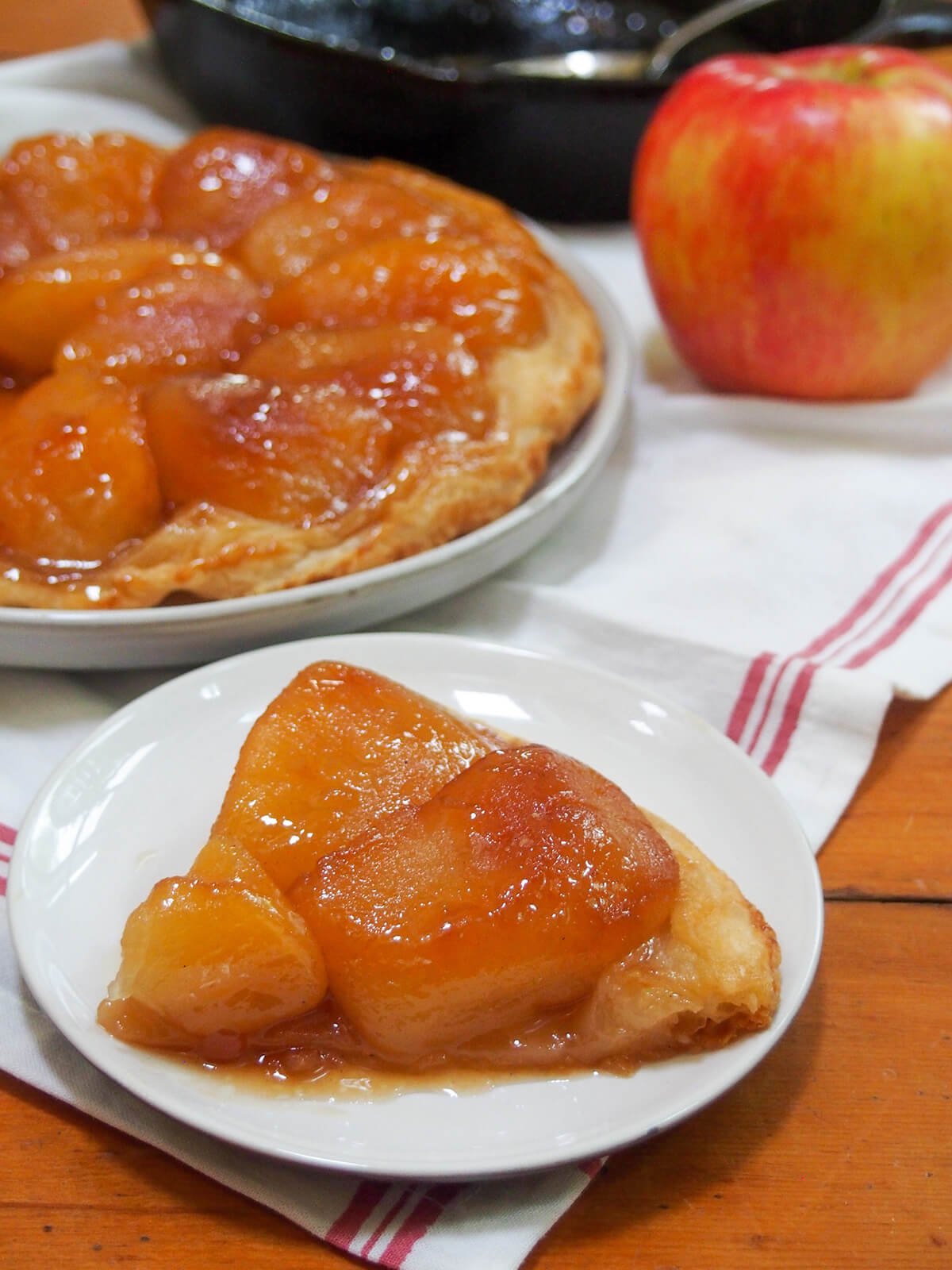 Apple tarte tatin is a classic French dessert that tastes wonderfully indulgent, despite only a few ingredients. An upside down tart with luscious caramel-coated, tender apples and is oh so good. slice of apple tarte tatin in front of rest of tart and apple behind