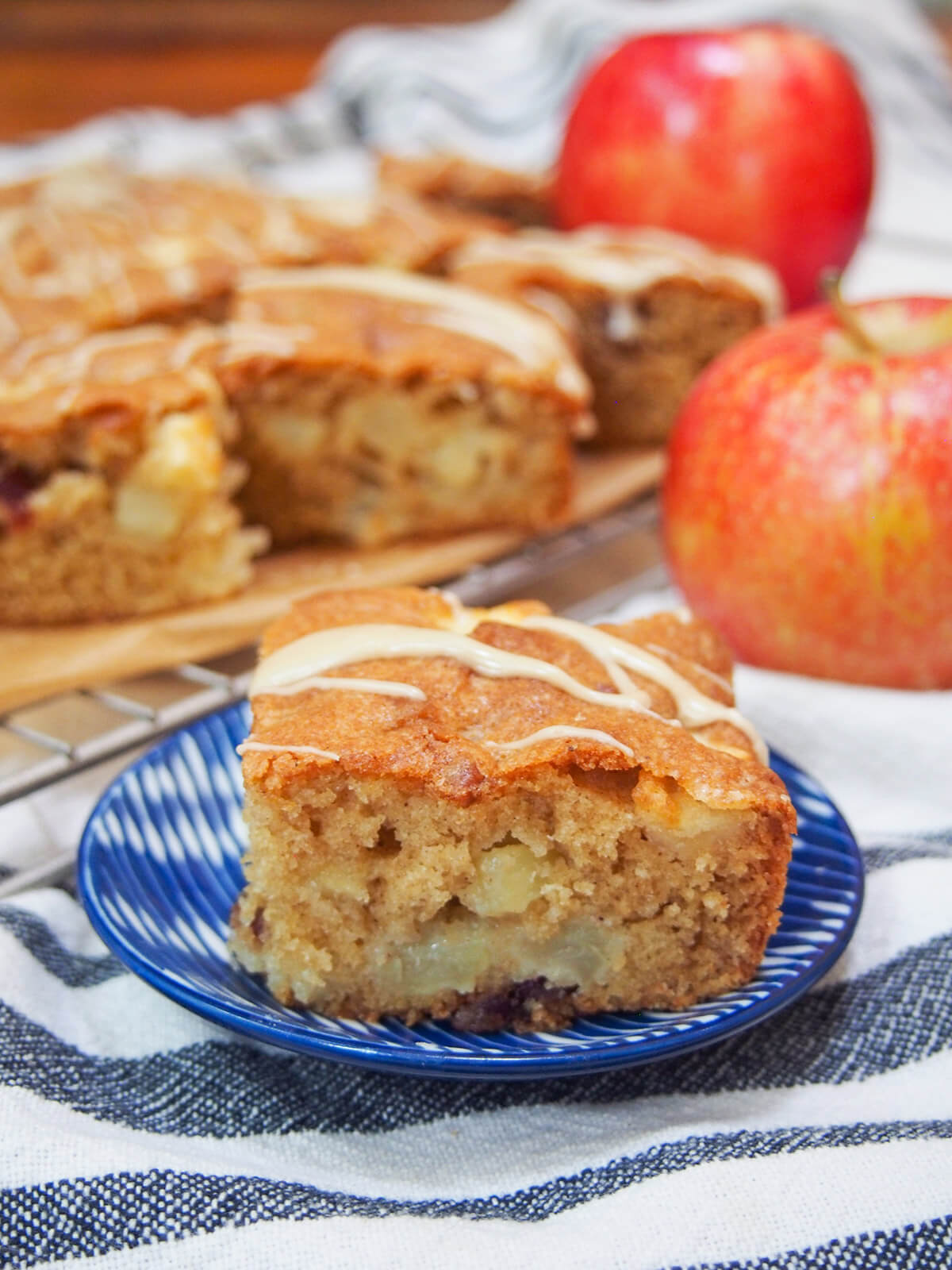 This apple snack cake is easy to make, packed with chunks of apple and gently spiced. It has a wonderful balance of sweetness, tender buttery cake and fruitiness. It's always incredibly popular with all who try it, so make sure you do soon, too! slice of apple snack cake on small plate with more behind