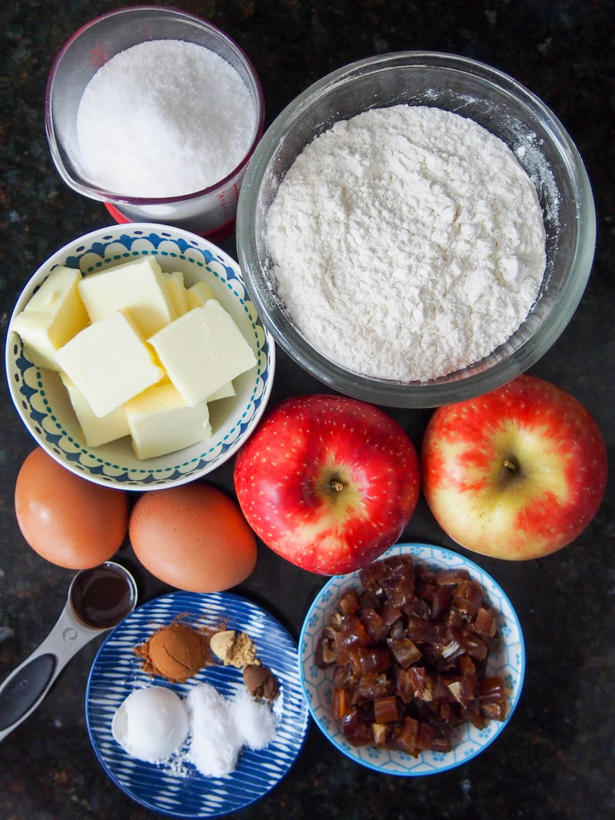bowls with flour, sugar, butter, apples, eggs, dates and spices