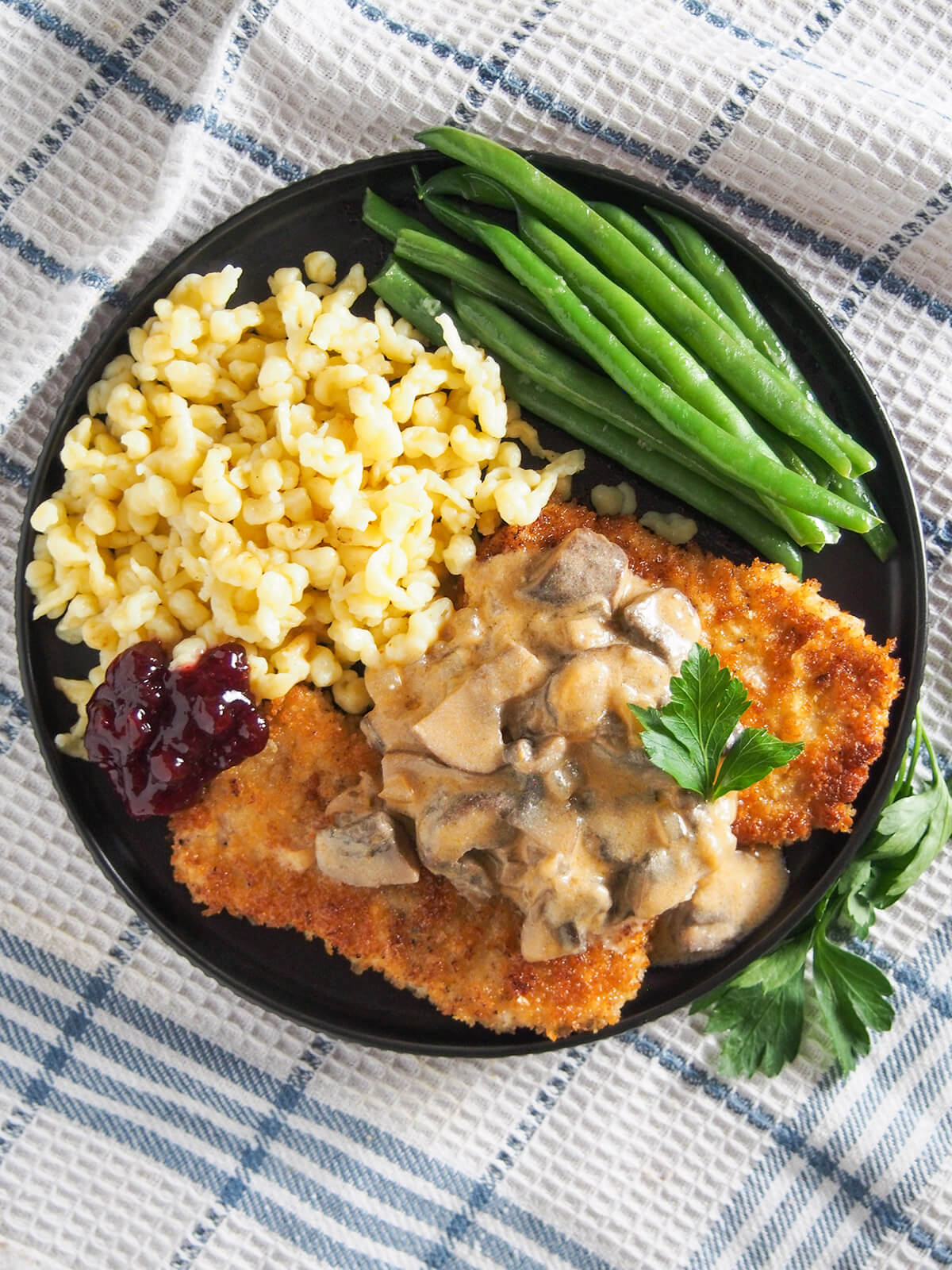 overhead view of plate of jaegerschnitzel with spaetzle and beans