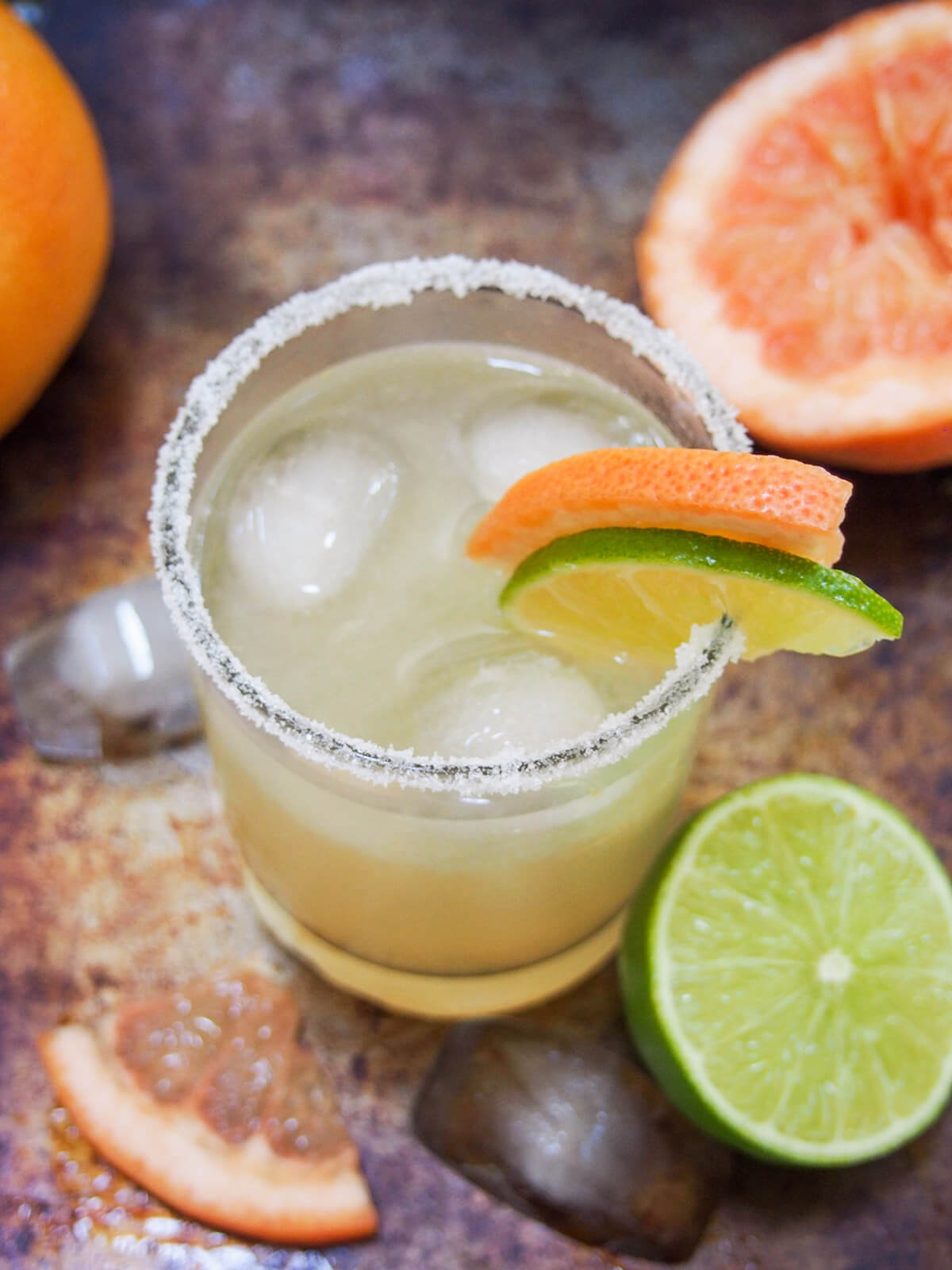 The Paloma cocktail is a wonderfully easy classic tequila-based cocktail. Made with fresh grapefruit juice gives it a bright, fresh flavor profile - a perfect balance of sweet and tart flavors, and wonderful to sip on. glass of paloma cocktail with salt rim and fruit garnish with cut lime and grapefruit to side