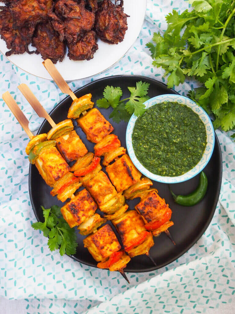 plate with skewers of paneer tikka with bowl of green chutney on the side