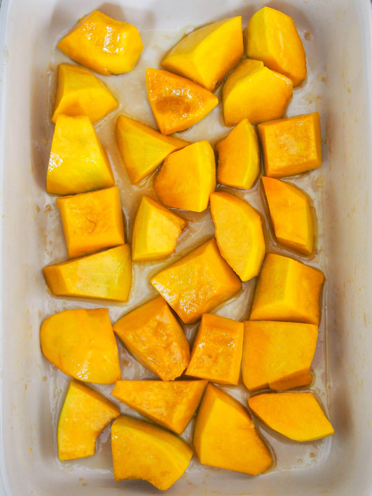 diced squash in baking dish tossed with oil and maple syrup