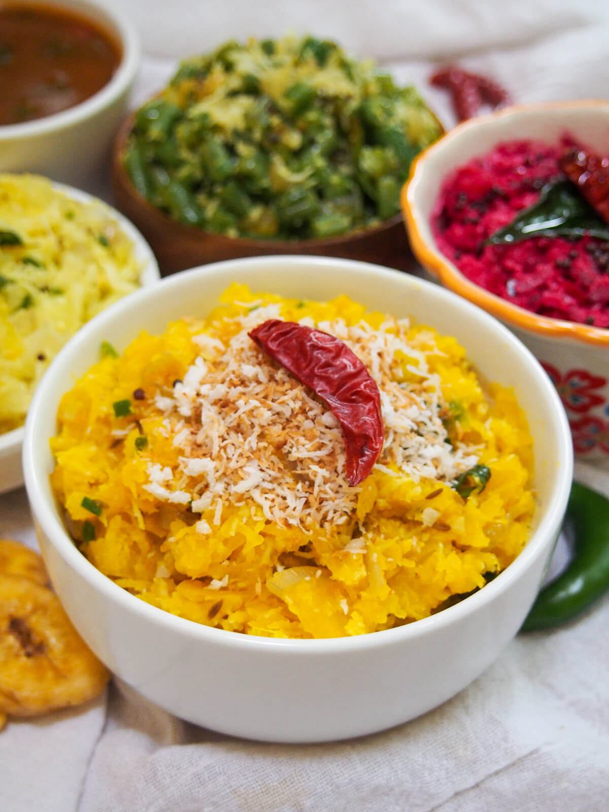 bowl of pumpkin erissery with colorful thorans and pachadi behind