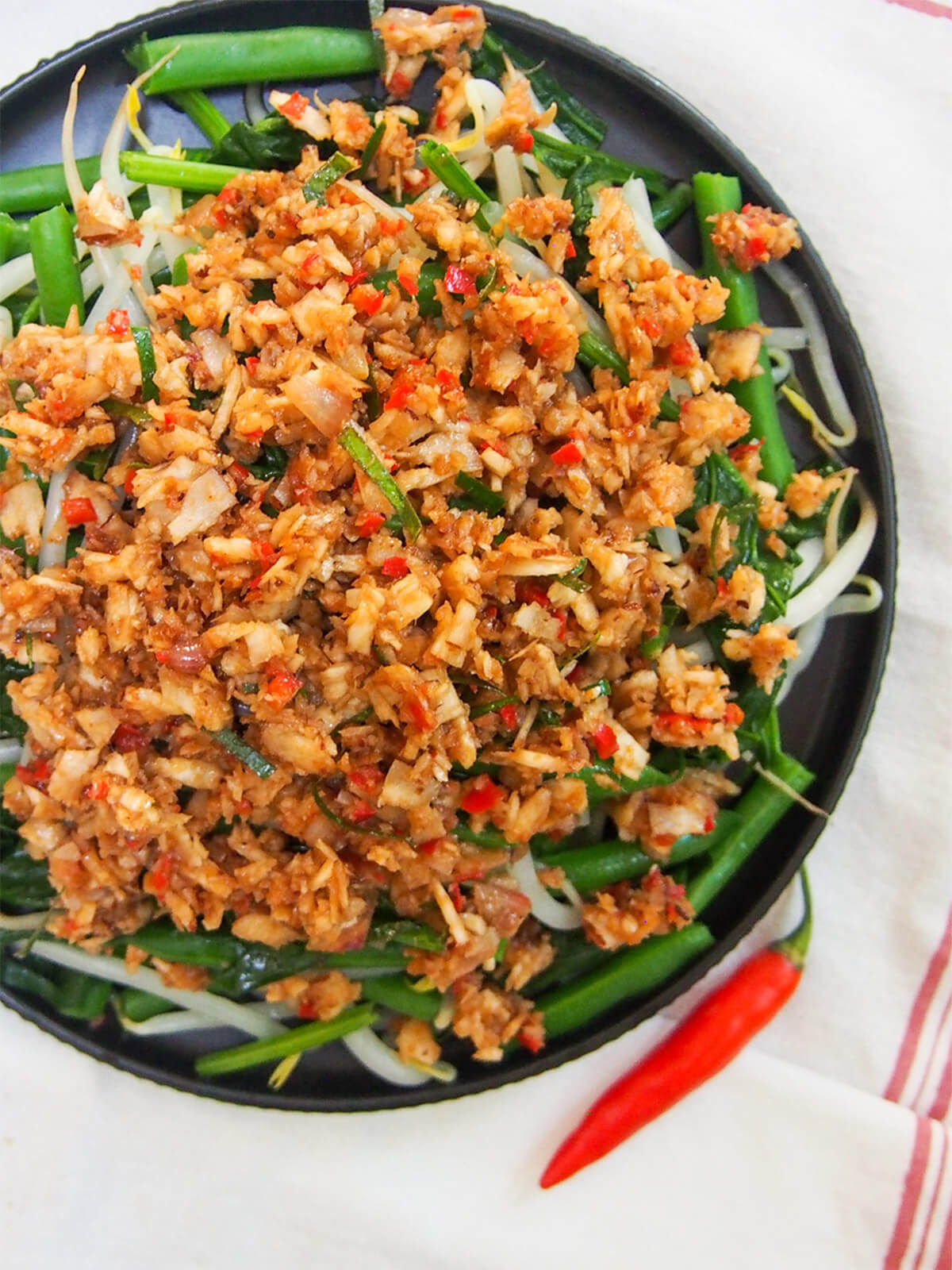 Urap sayur is a popular Indonesian dish combining blanched vegetables with a spiced coconut topping. It's easy to make with a delicious combination of spicy, sweet and sour flavors. plate of Urap sayur (Indonesian vegetables with coconut topping) from overhead