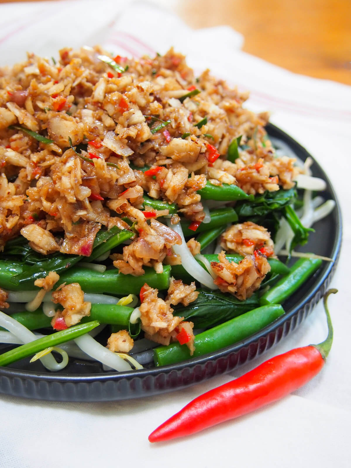 Urap sayur is a popular Indonesian dish combining blanched vegetables with a spiced coconut topping. It's easy to make with a delicious combination of spicy, sweet and sour flavors. side view of plate of urap sayur (Indonesian vegetables with coconut topping)