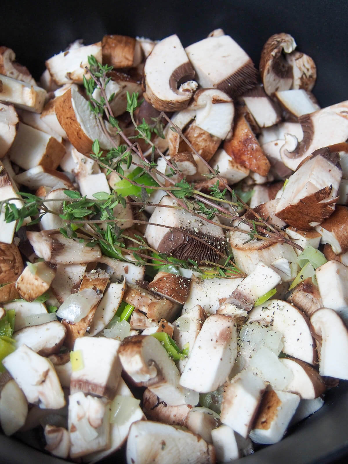 adding mushrooms for wild mushroom soup chopped mushrooms with herbs on top in pot