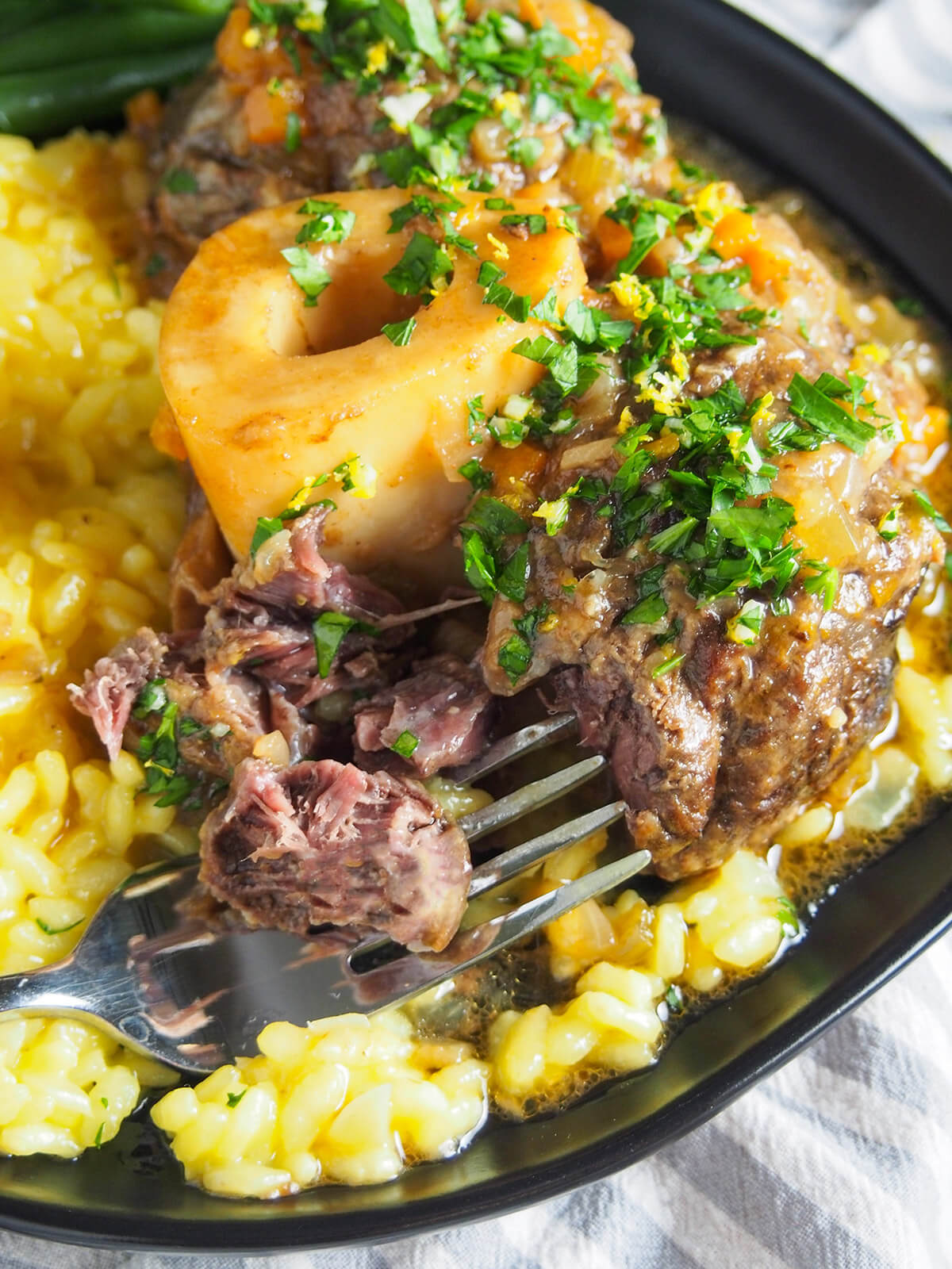 Osso buco is a traditional slow cooked Italian dish. Traditionally made with veal, this beef version has the same delicious meltingly tender meat and bright gremolata finish. Perfect comfort food. fork pulling apart beef osso buco