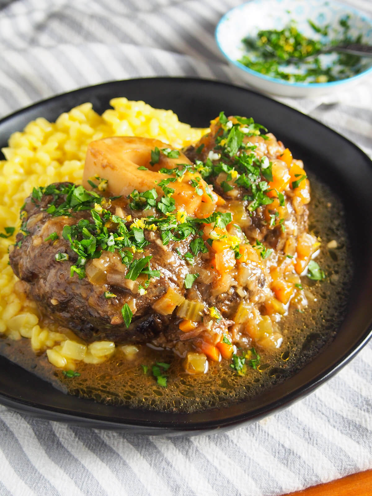 Osso buco is a traditional slow cooked Italian dish. Traditionally made with veal, this beef version has the same delicious meltingly tender meat and bright gremolata finish. Perfect comfort food. plate of beef osso buco over saffron risotto