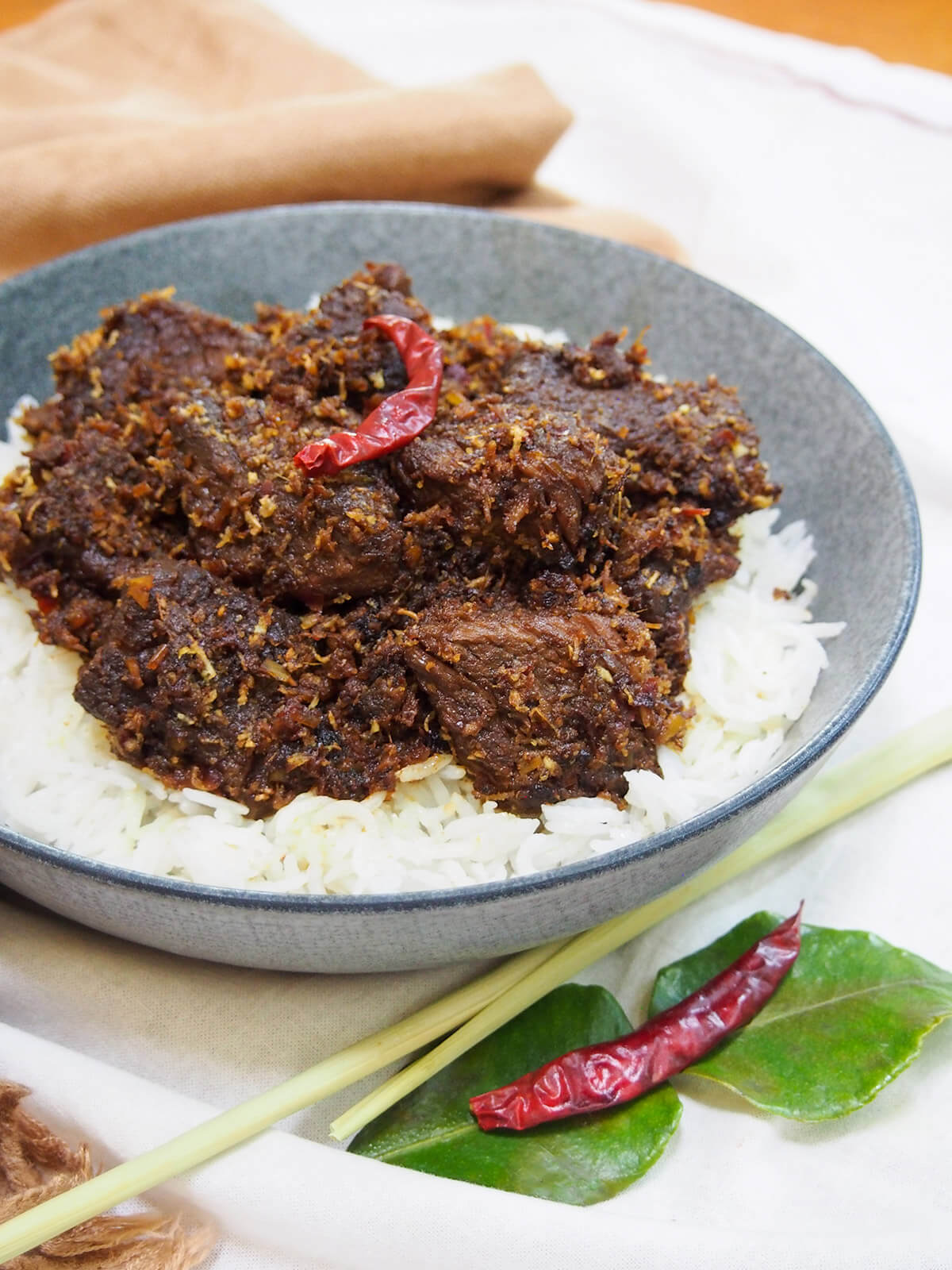 bowl of beef rendang from side with spices below bowl