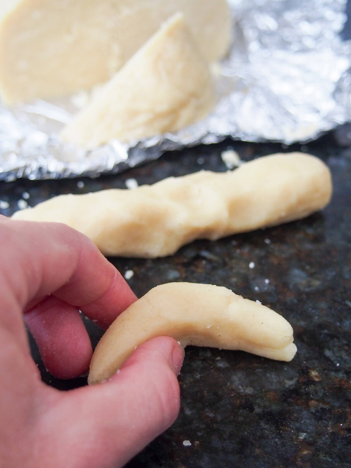forming vanilla crescent cookie shape forming crescent shape with piece of cookie dough with more dough behind