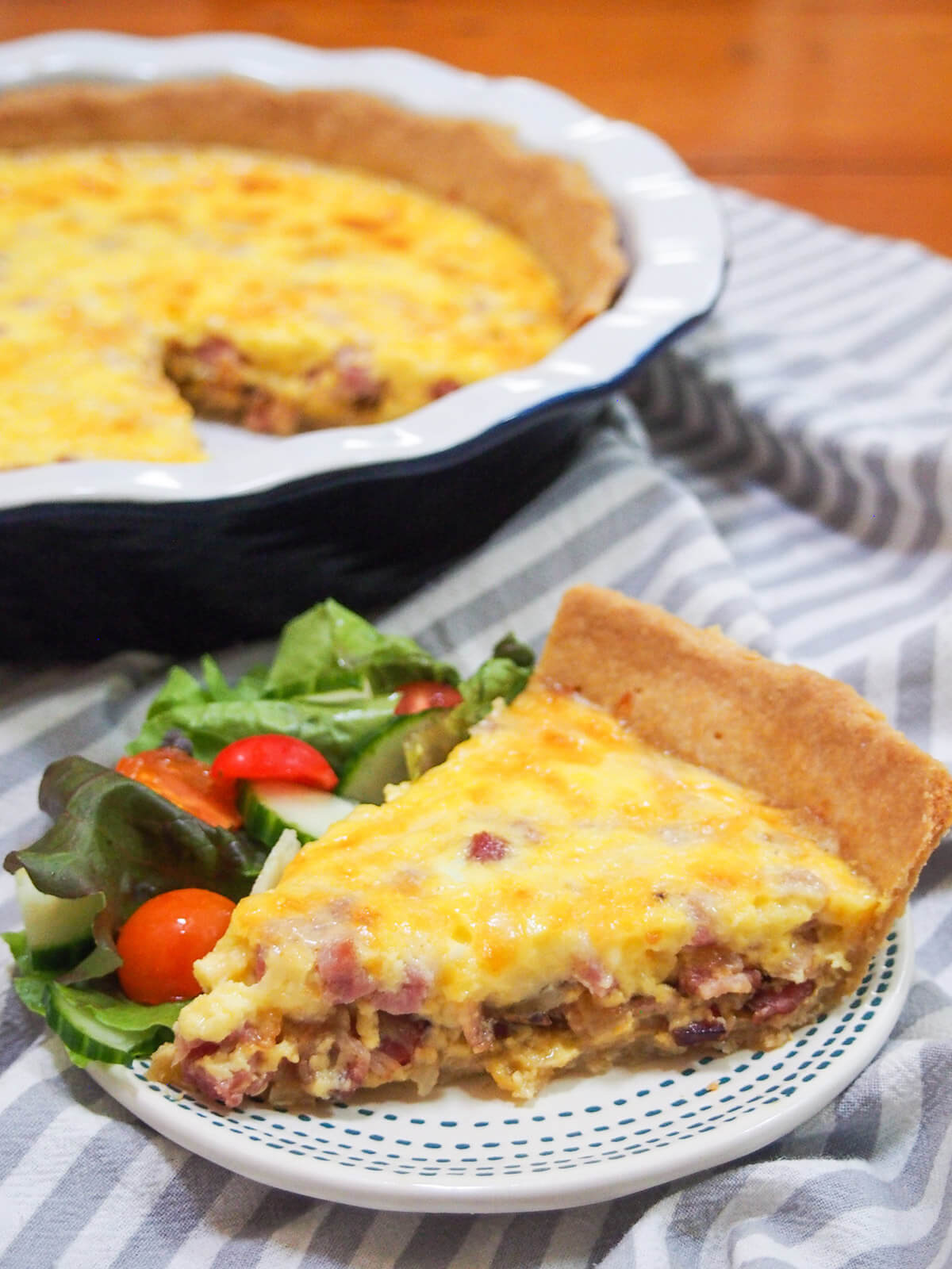 slice of quiche Lorraine on plate in front of rest of quiche in pie dish