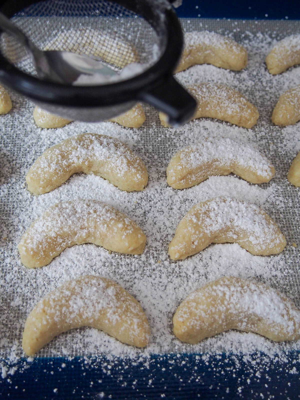 dusting vanillekipferl with powdered sugar sifting vanilla powdered sugar over warm cookies