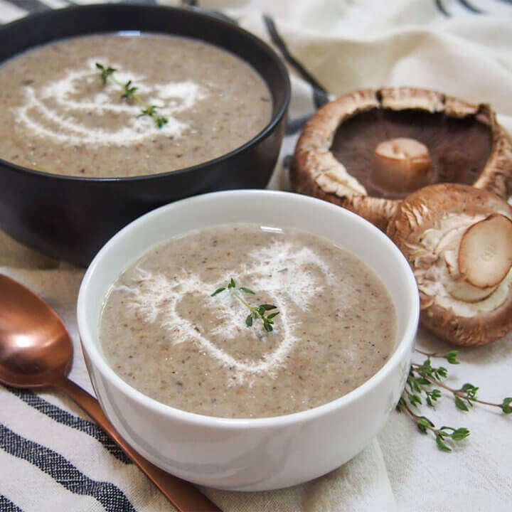 bowl of wild mushroom soup with another bowl and mushrooms part in view behind
