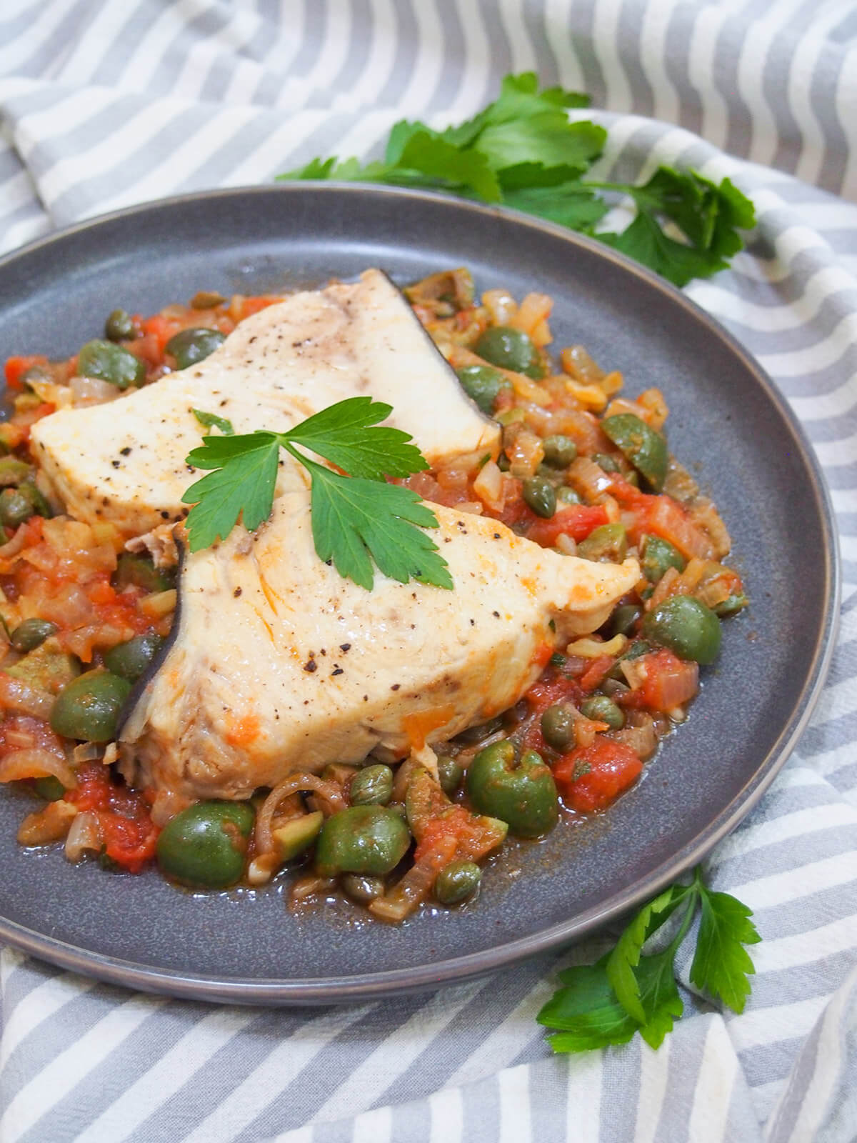 two pieces of swordfish over olive, caper and tomato sauce