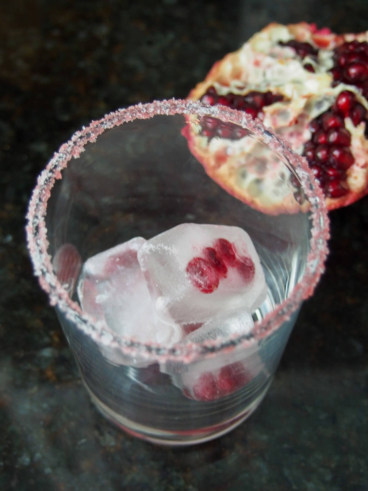 glass with salt rim and ice cubes inside with pomegranate seeds in them
