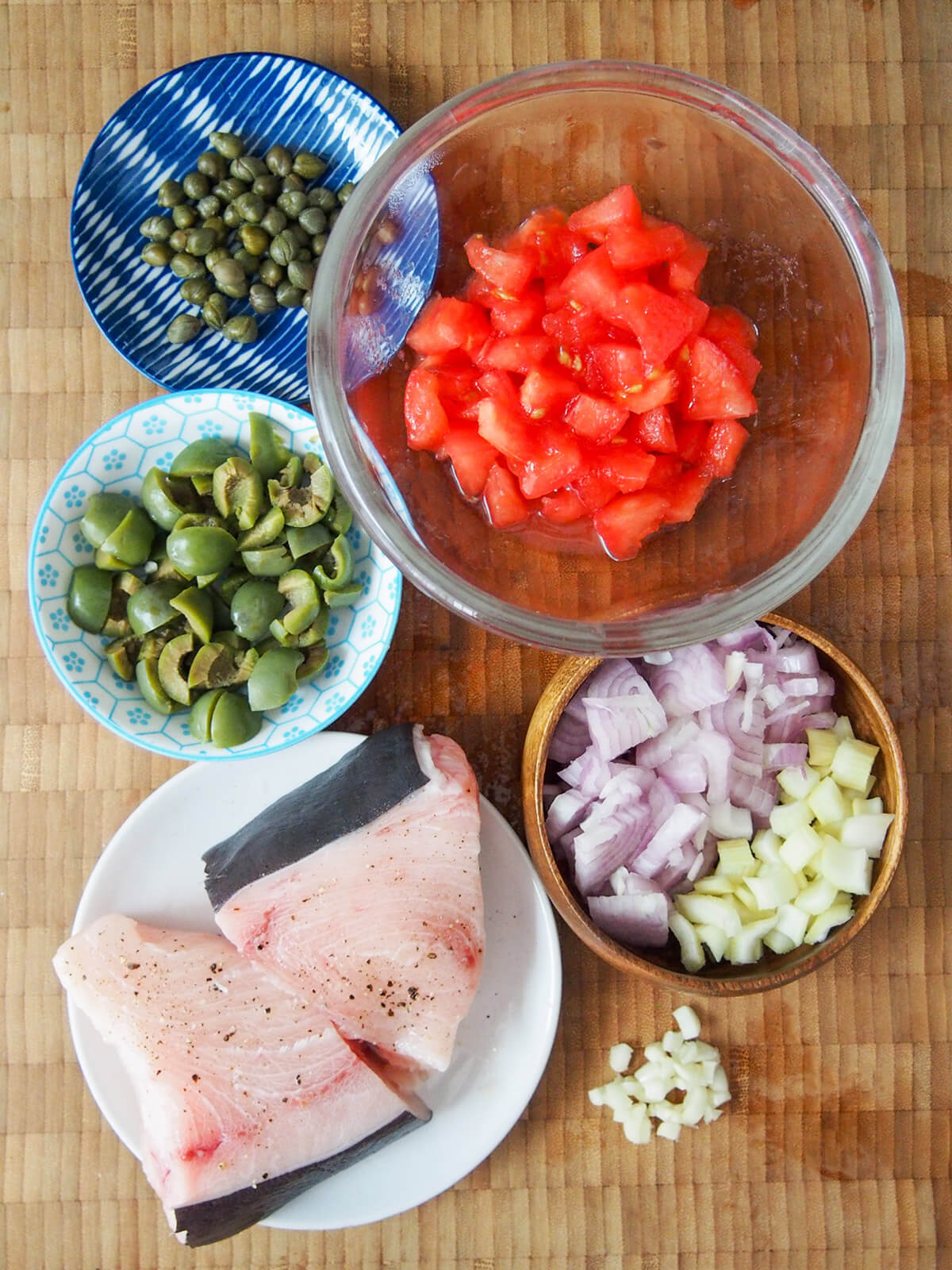 plate of swordfish and bowls with olives, capers, tomatoes, onions