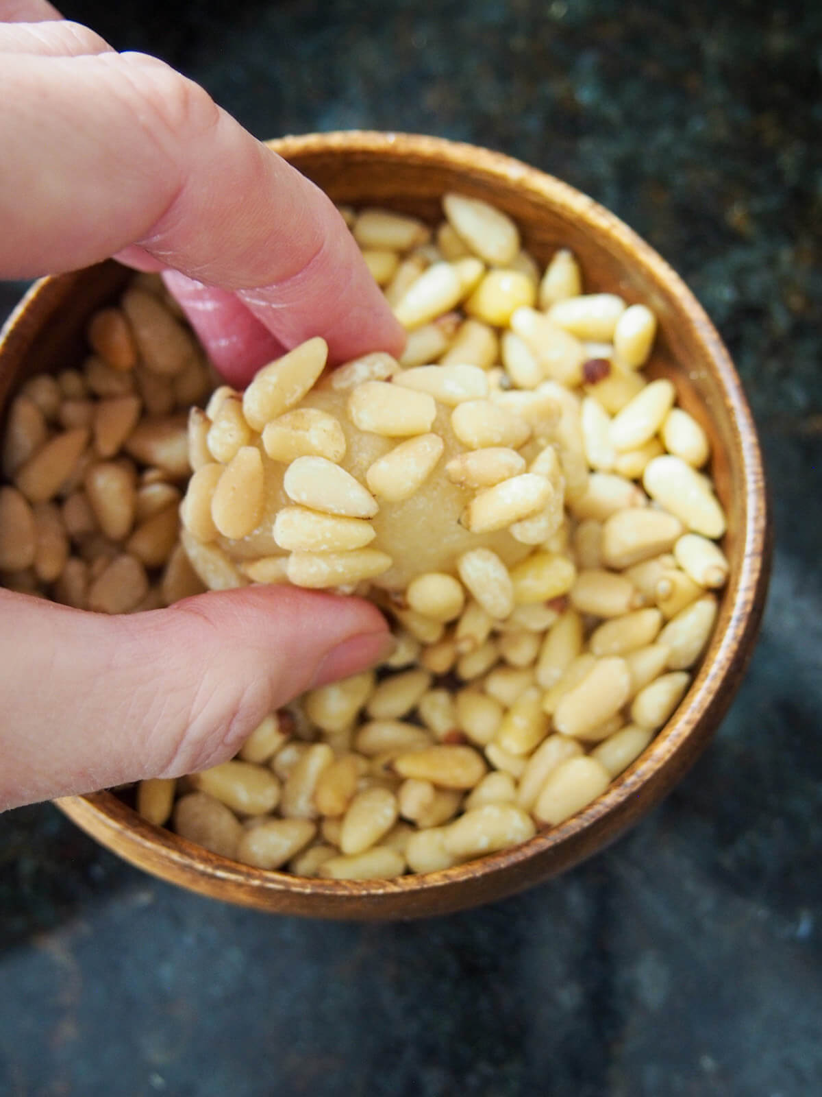 rolling cookie in bowl of pine nuts