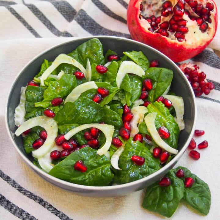bowl of spinach pomegranate salad with some pomegranate to side and behind