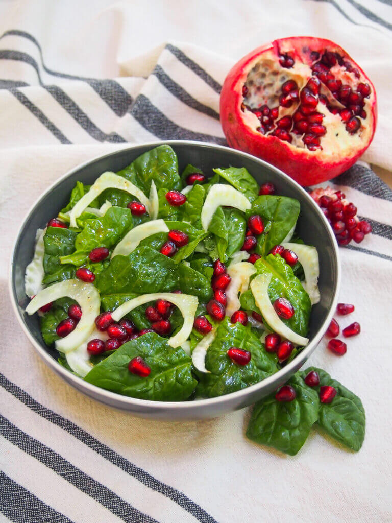 spinach pomegranate salad in bowl with pomegranate behind