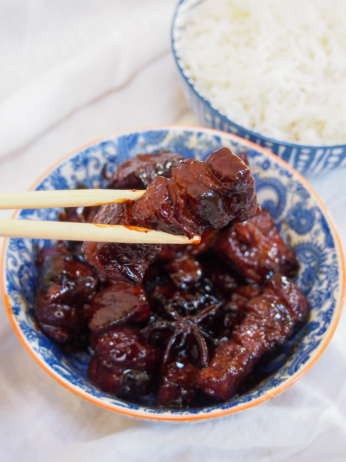 holding a piece of pork belly with chopsticks over bowl